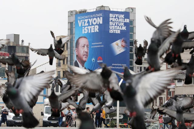 Pigeons fly in front of a large election poster of Turkish President Tayyip Erdogan in Istanbul