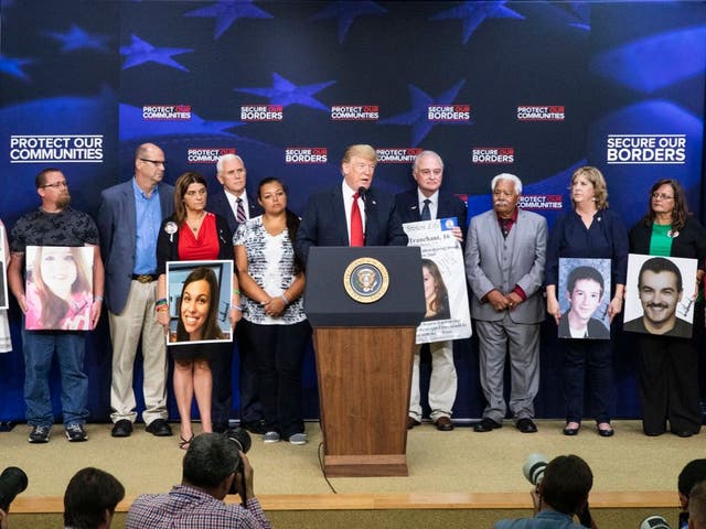 Donald Trump stands on stage with families of murder victims holding photos autographed by the president