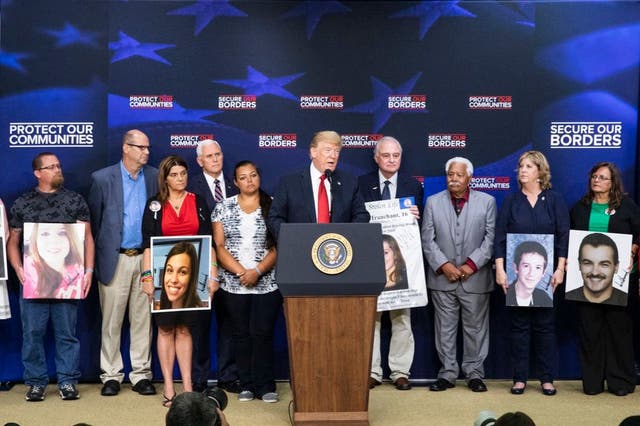 Donald Trump stands on stage with families of murder victims holding photos autographed by the president