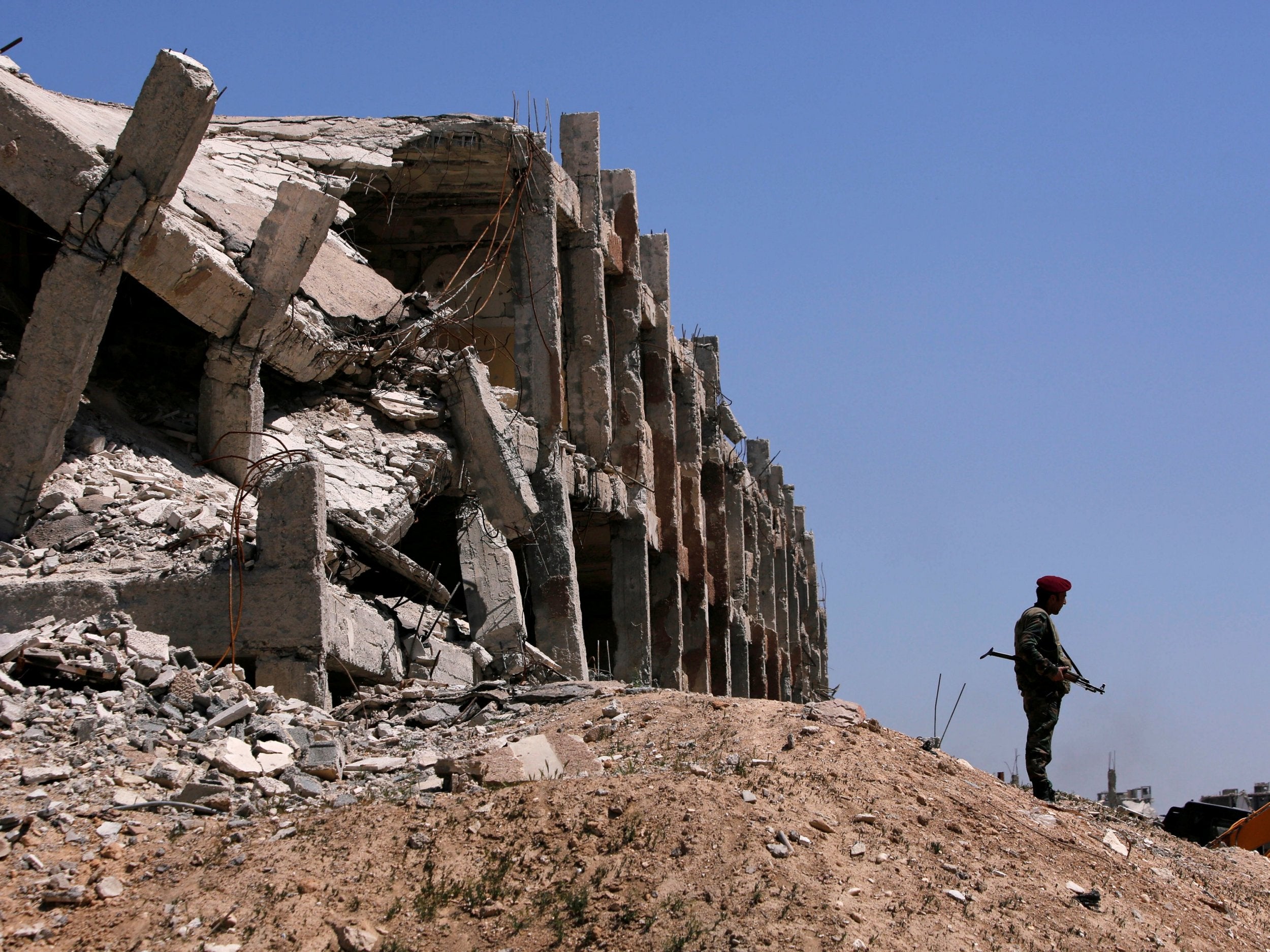 A Syrian government soldier stands guard near destroyed buildings in Jobar, Damascus