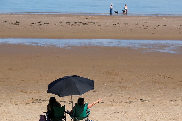 People sit under an umbrella on the beach in the sunshine in Liverpool