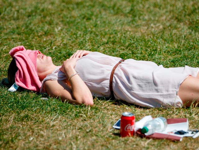 A woman shelters from the sun as she lies in Green Park, London, on Monday