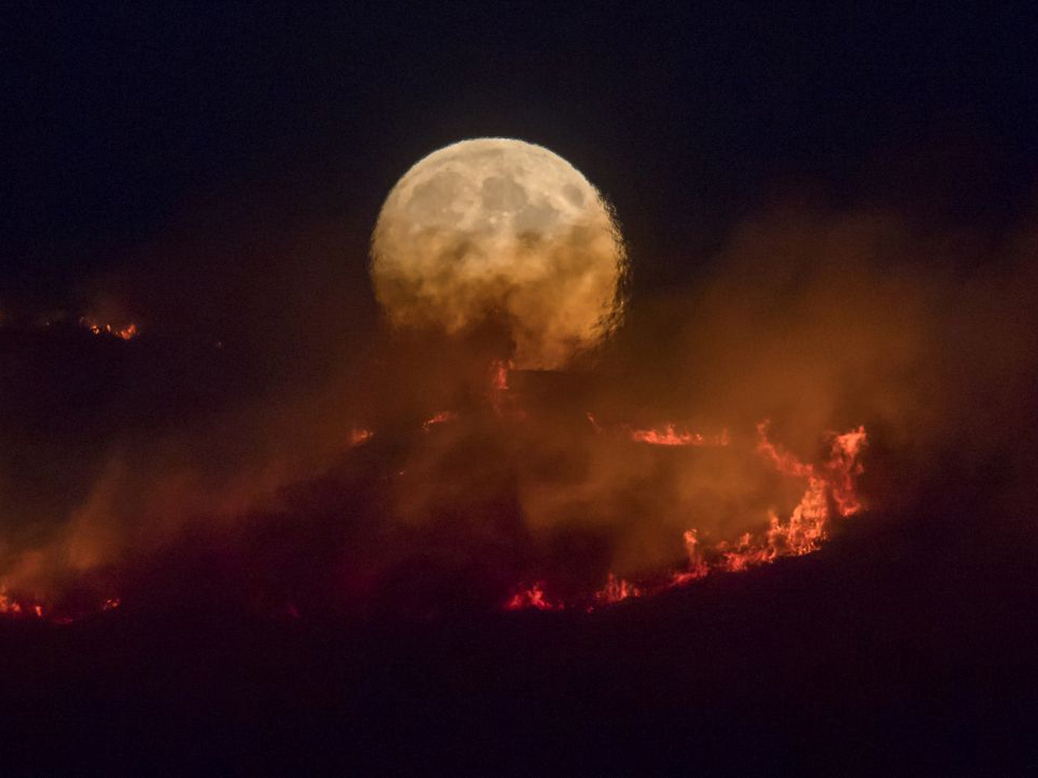 The full moon rises behind burning moorland as a large wildfire spreads across Saddleworth (Getty)