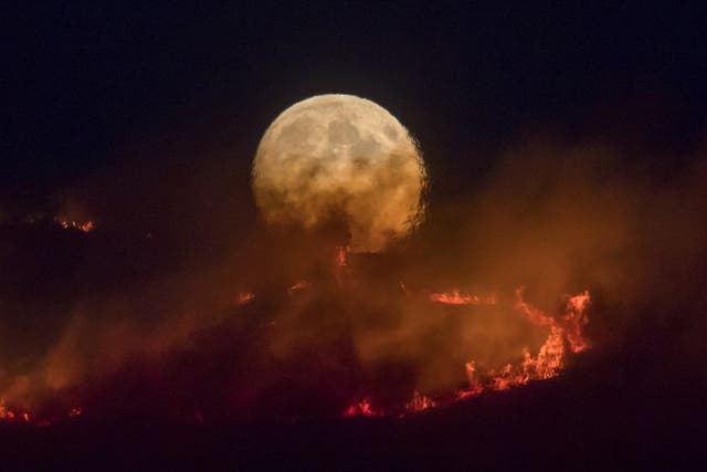 The full moon rises behind burning moorland as a large wildfire spreads across Saddleworth