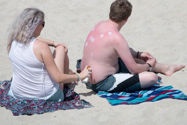 A woman applies sun lotion to a man's back as they enjoy the fine weather on Porthmeor Beach, St Ives, on Thursday
