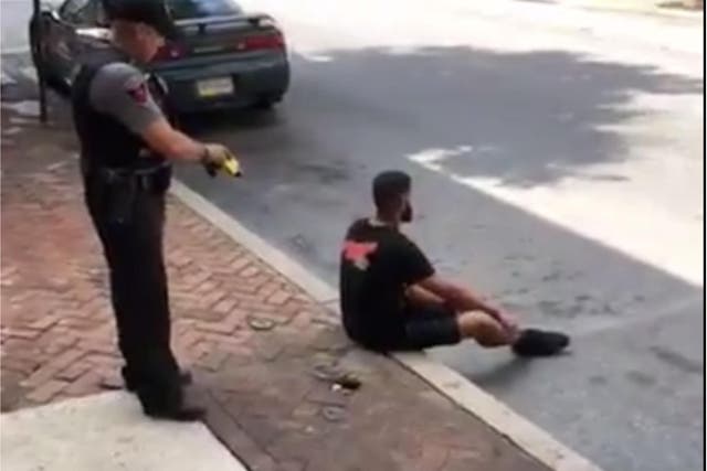 The video shows the man sitting on a curb before he is tased