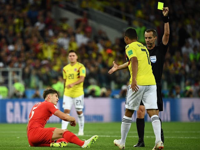 Referee Mark Geiger gives a yellow card to Colombia's Carlos Bacca as he walks towards England's John Stones
