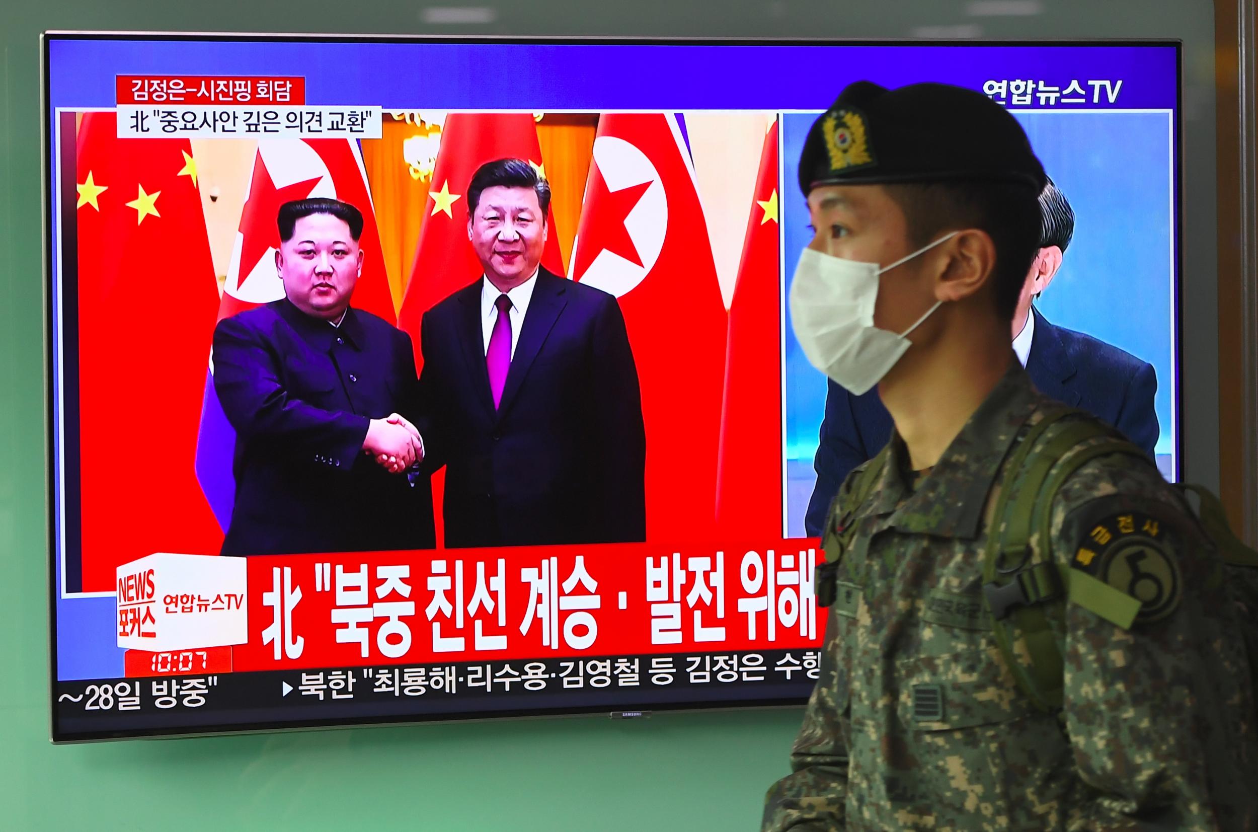 A South Korean soldier walks past a television news screen reporting about a visit to China by North Korean leader Kim Jong Un