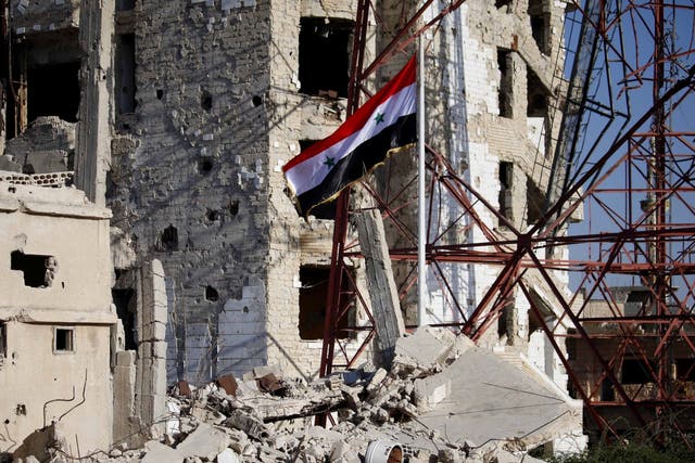 The Syrian national flag rises in the midst of damaged buildings in Deraa