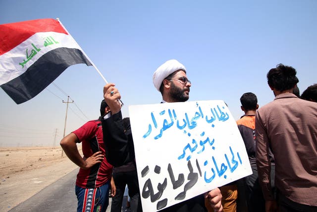 A protester holds a sign that reads ‘We ask the decisionmakers to provide the things we are deprived of’, during a demonstration south of Basra