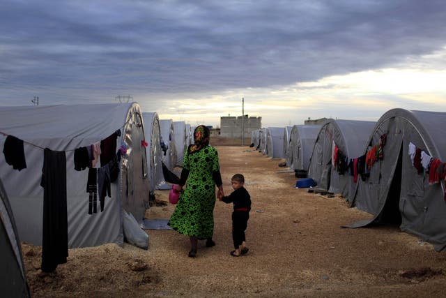 A Syrian woman and her child walk beside their tent in a camp in the southeastern town of Suruc on the Turkish-Syrian border in this file photo from 2014