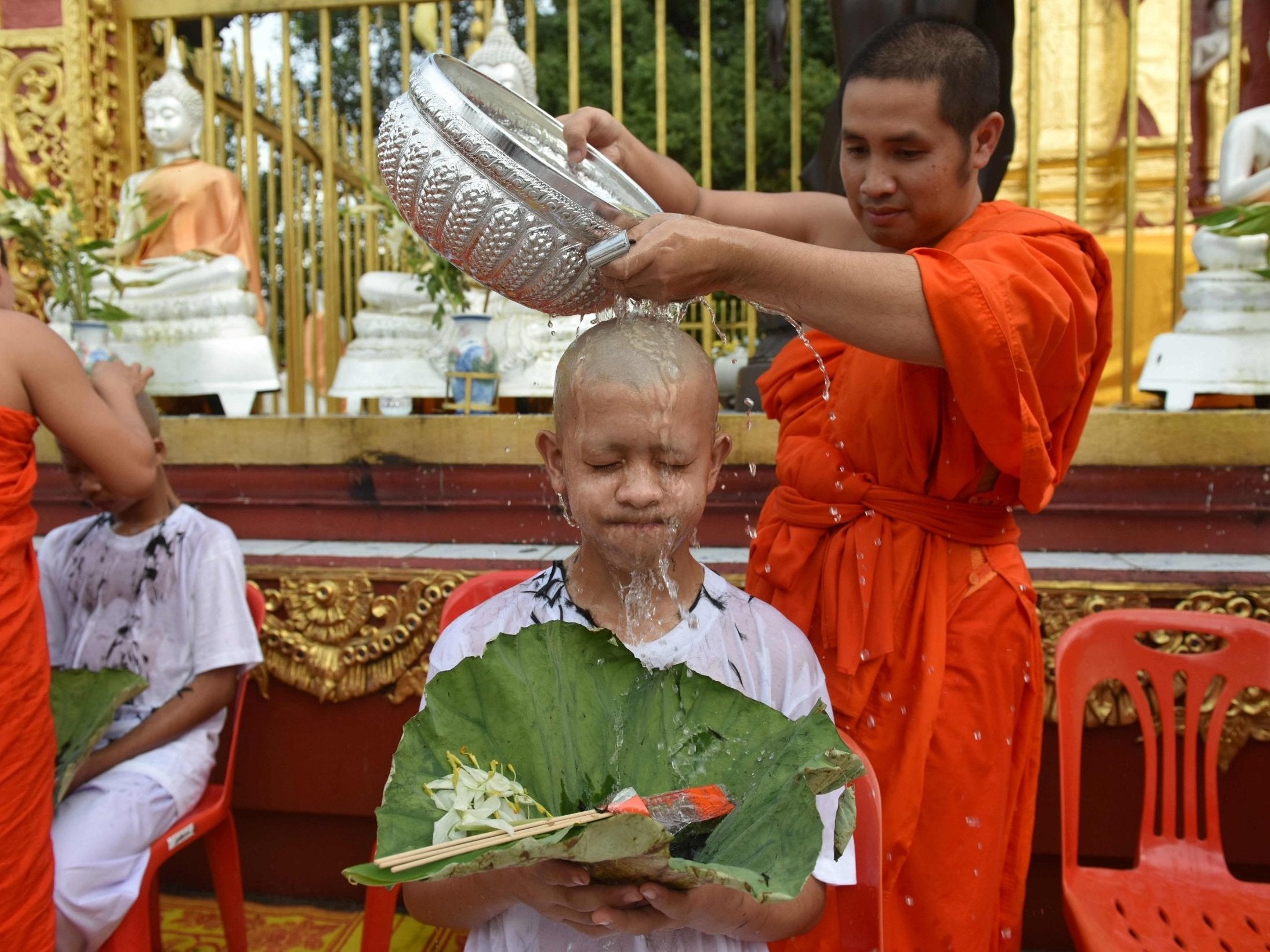 A Buddhist monk bathes the shaved head of the rescued Thai boy and a member of 'Wild Boars' football team
