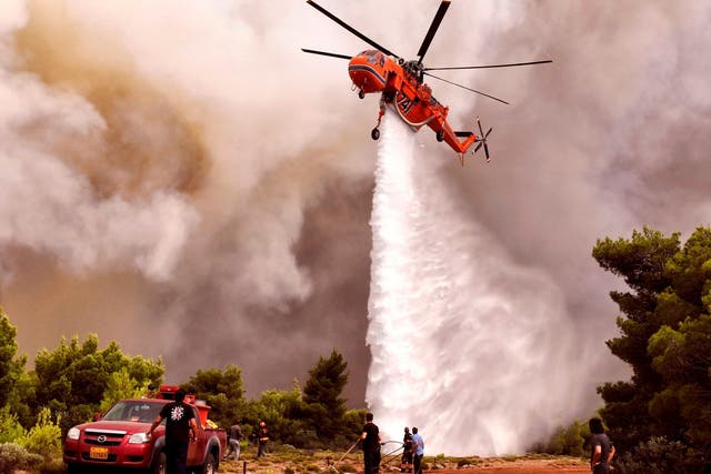 A firefighting helicopter drops water to extinguish flames during a wildfire at the village of Kineta, near Athens, on 24 July