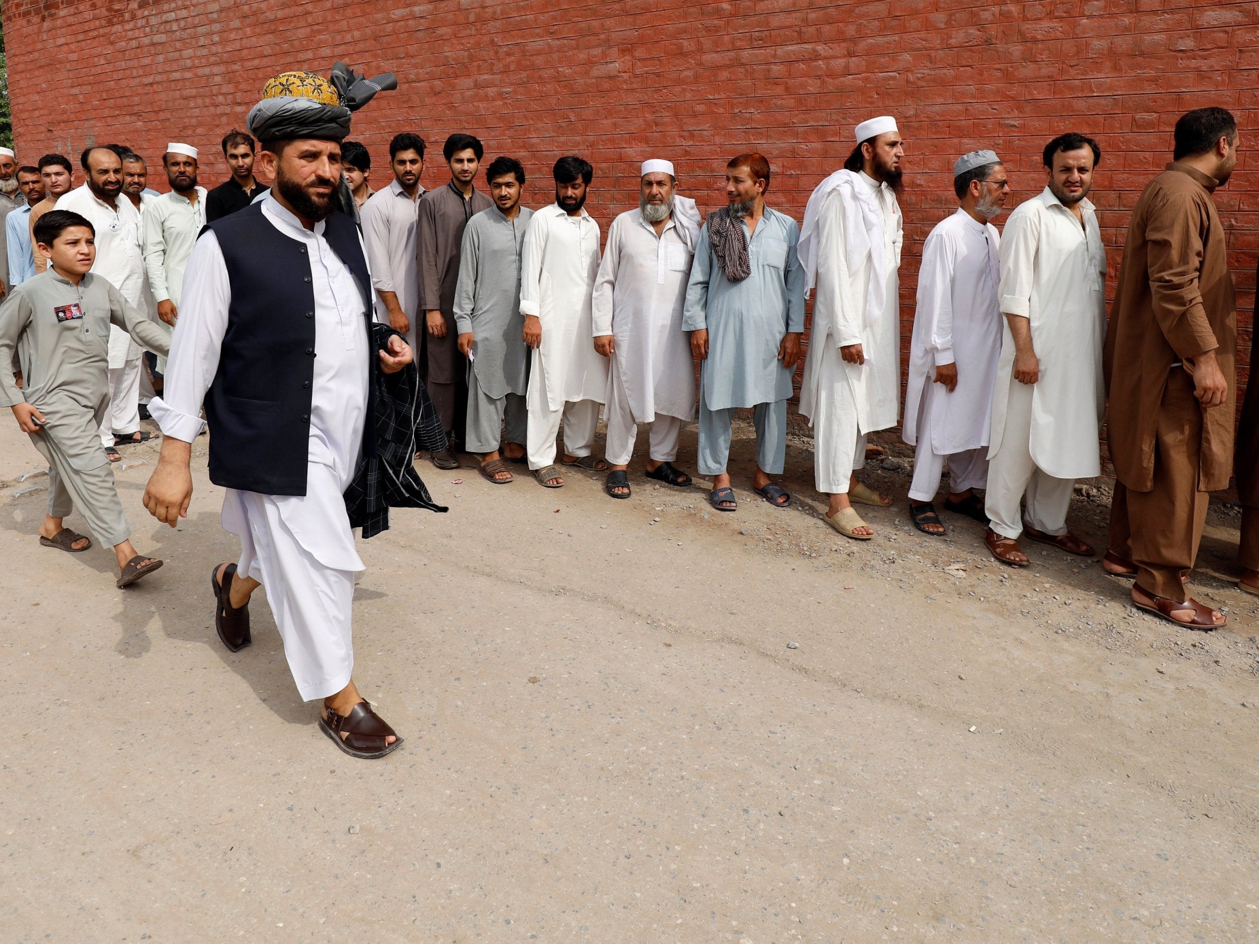Men stand in line to cast their vote during the general election in Peshawar
