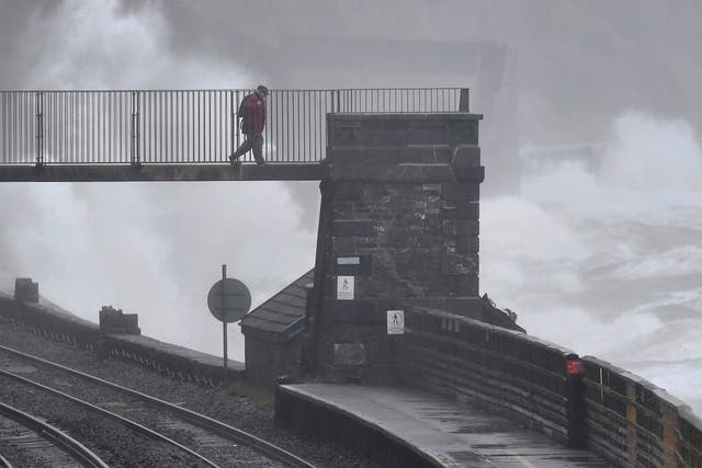 Large waves hit the sea wall as a man walks over the railway line at Dawlish
