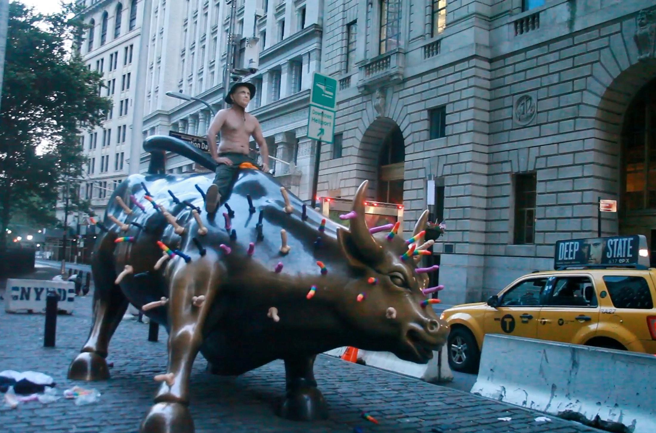 Activist Jeff Jetton, bare chested and wearing a mask to portray Russia's President Vladimir Putin, sits on the Wall Street bull sculpture covered with sex toys in a still image from video taken in New York City, U.S. July 16, 2018.