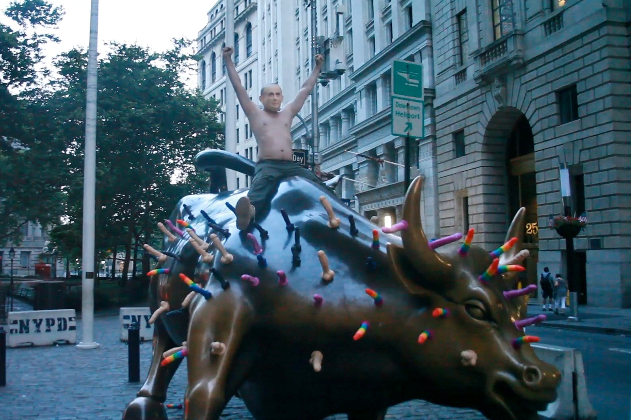Activist Jeff Jetton, bare chested and wearing a mask to portray Russia's President Vladimir Putin, sits on the Wall Street bull sculpture covered with sex toys in a still image from video taken in New York City, U.S. July 16, 2018.