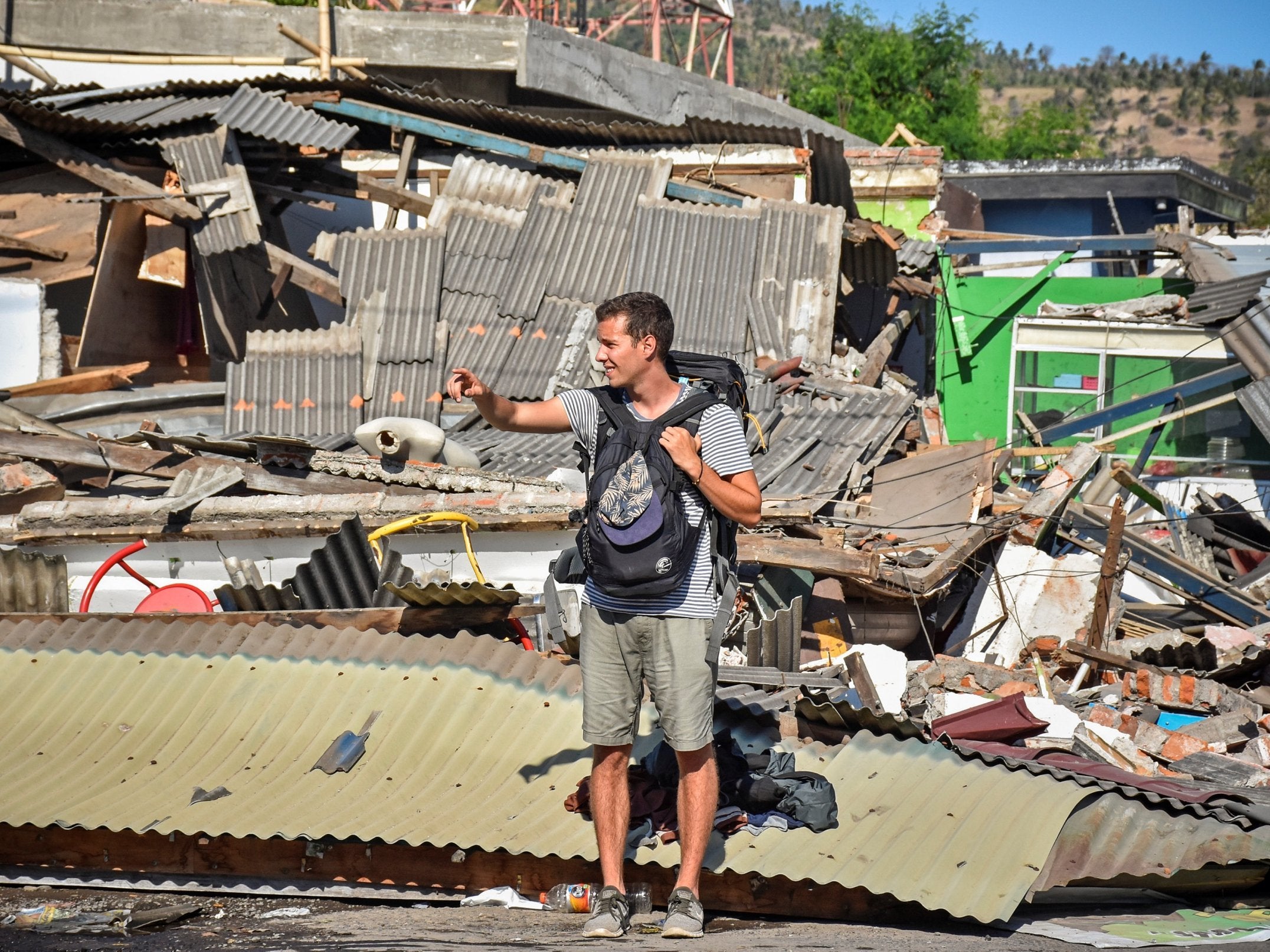 A tourist stands near damaged buildings as he tries to flag down a car after the earthquake (Antara Foto/Ahmad Subaidi/ via Reuters)