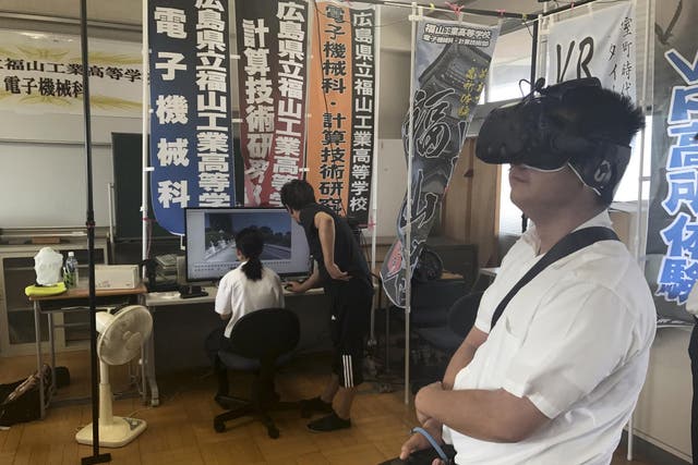 Namio Matsura, right, a 17-year-old member of the computation skill research club at Fukuyama Technical High School, watches Hiroshima before the fall of the atomic bomb in virtual reality experience