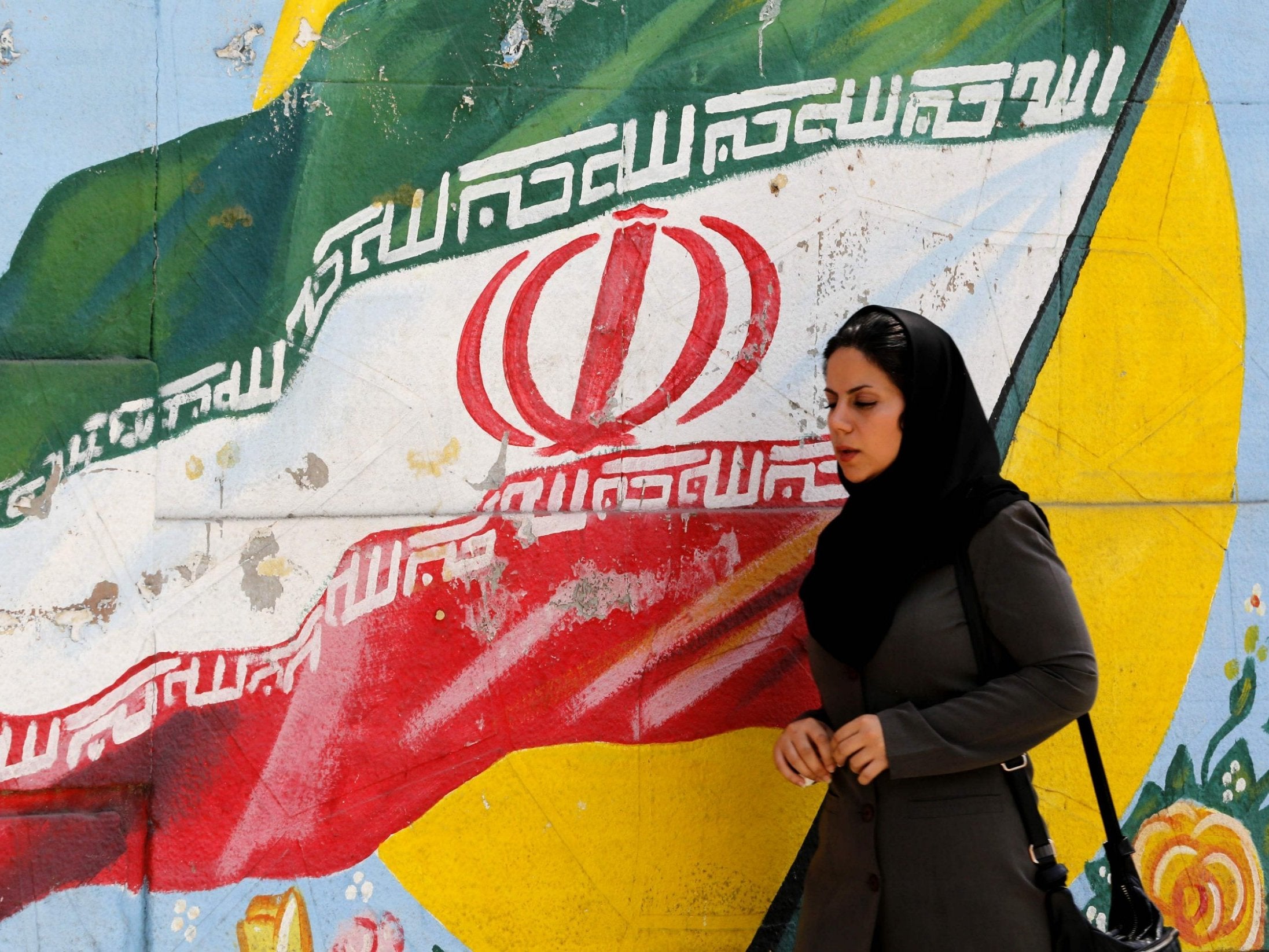 A woman walks in front of a mural painting depicting the Iranian flag, in the capital Tehran on August 6, 2018.