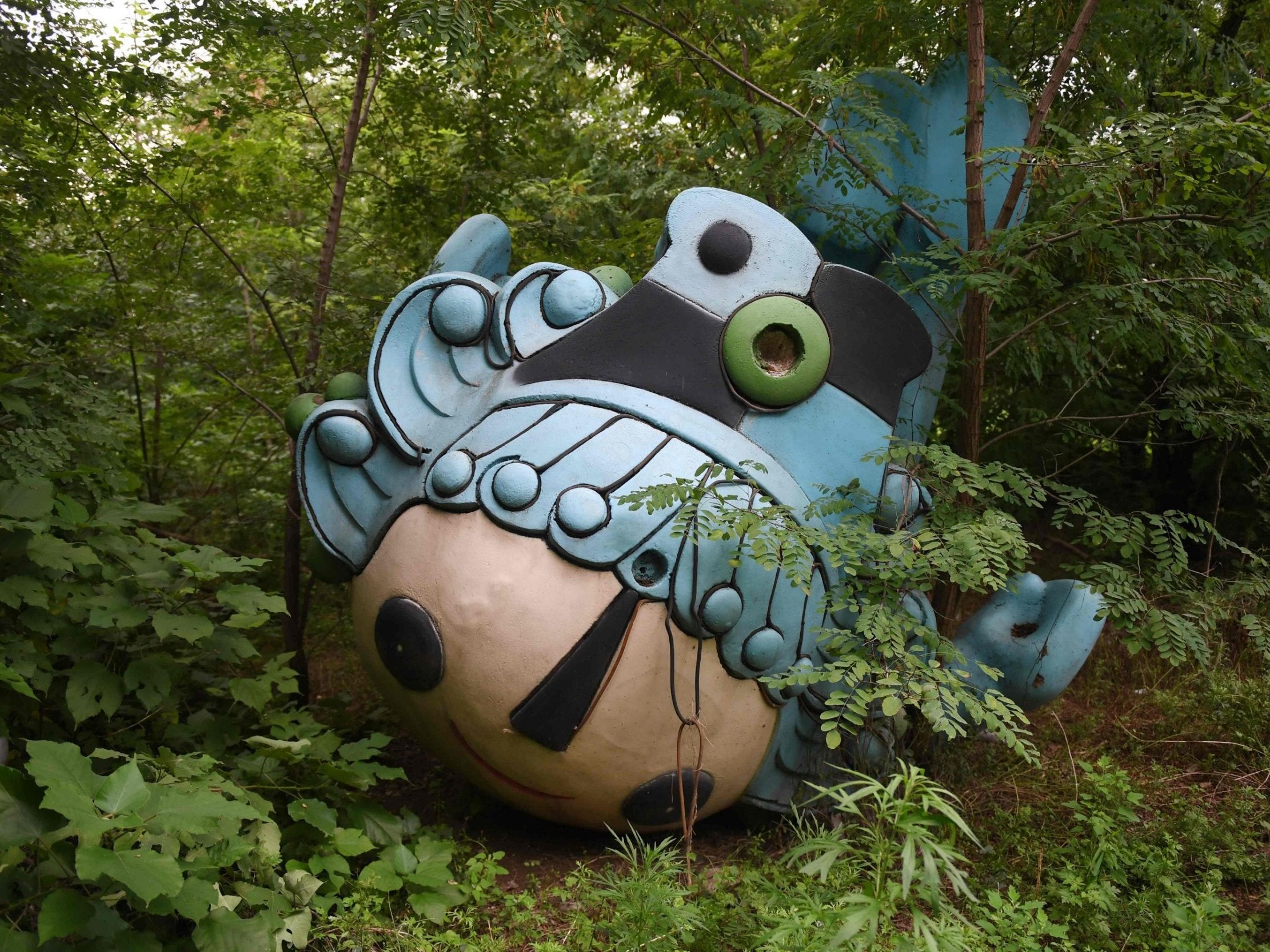 Beibei, one of five mascots for the 2008 Beijing Olympic Games, lying amongst trees behind an abandoned, never-completed mall in Beijing