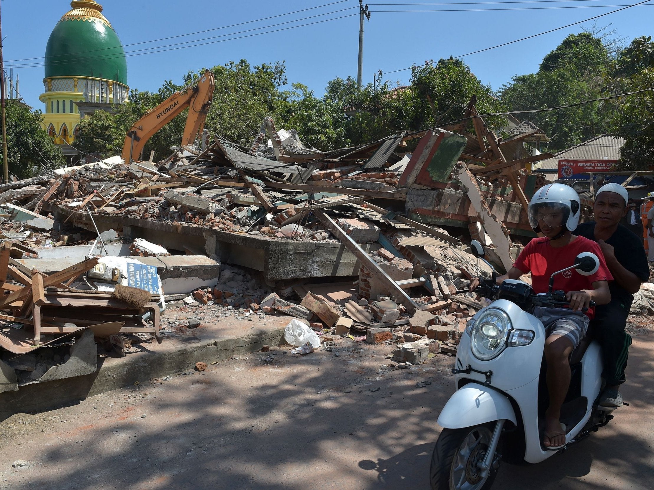 Indonesian motorists ride past collapsed buildings after a recent quake in Tanjung on Lombok island