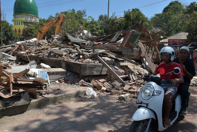Indonesian motorists ride past collapsed buildings after a recent quake in Tanjung on Lombok island
