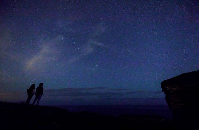 This picture taken on August 12, 2017 shows a couple enjoying Perseid meteor along the Milky Way illuminating the dark sky near Comillas, Cantabria community, northern Spain, during the "Perseids" meteor shower