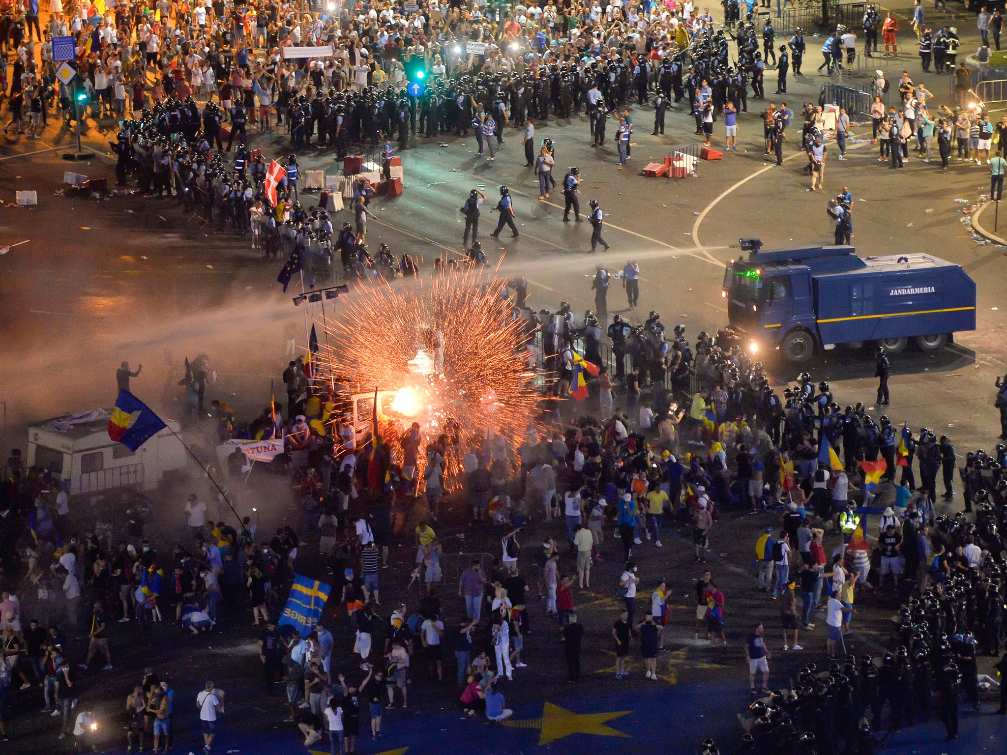 A teargas canister explodes as riot police charge using water canons to clear the square during protests outside the government headquarters in Bucharest