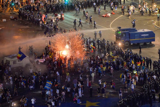 A teargas canister explodes as riot police charge using water canons to clear the square during protests outside the government headquarters in Bucharest