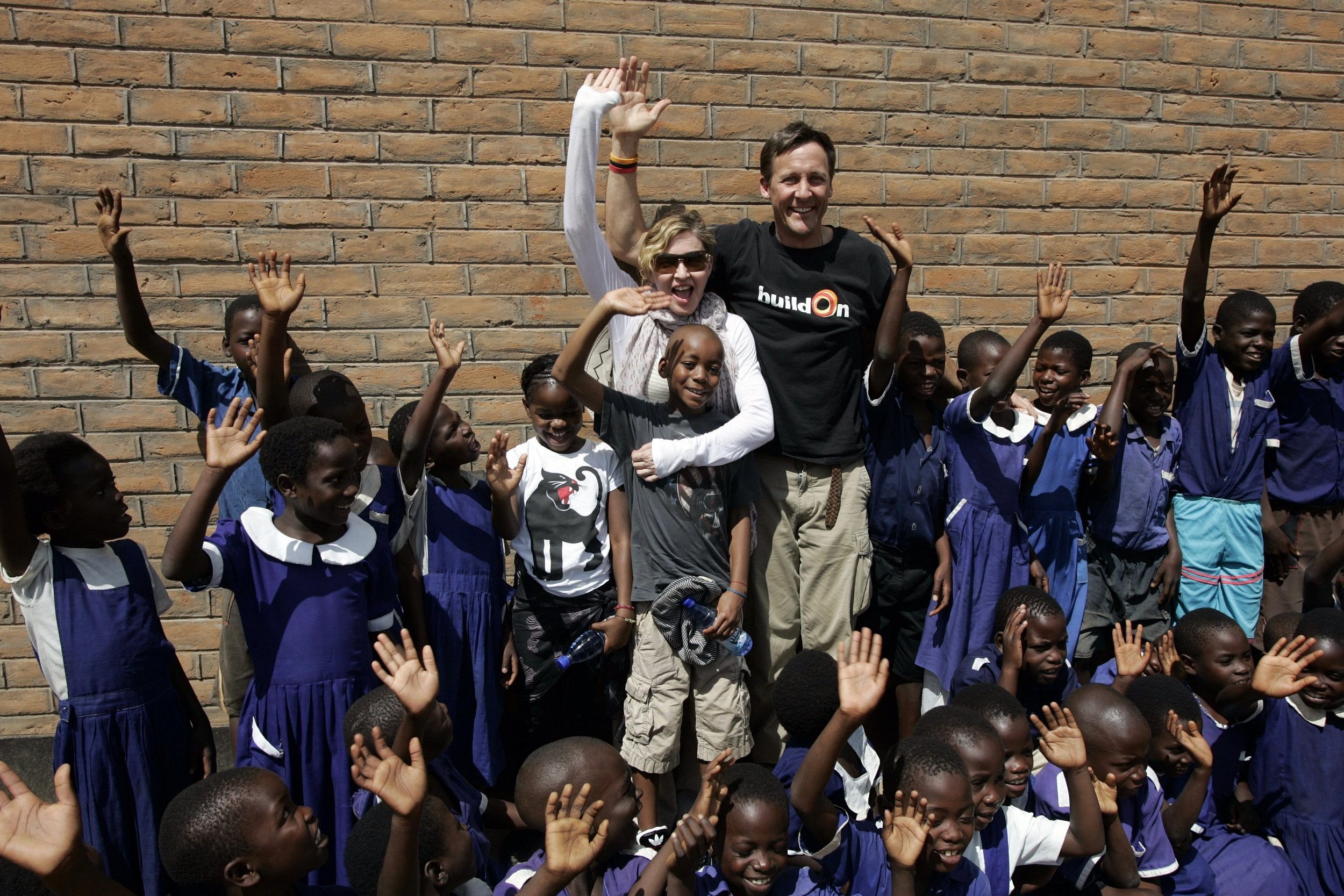 Madonna with her adopted children, David (in front of her) and Mercy (right) next to BuildOn CEO Jim Ziolkowski oustide of a classroom jointly built by her Raising Malawi organization