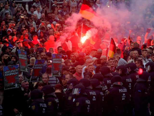 Far-right protesters brandish ‘Stop asylum’ placards at a rally in Chemnitz as a line of police officers watch on