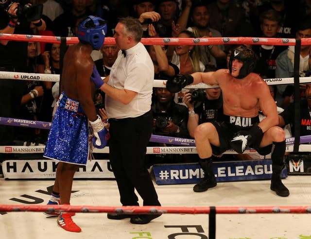 The referee holds back KSI as Logan Paul sits on the ropes