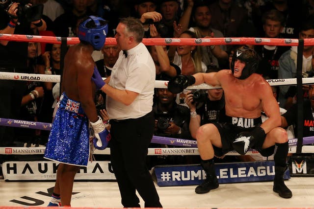 The referee holds back KSI as Logan Paul sits on the ropes