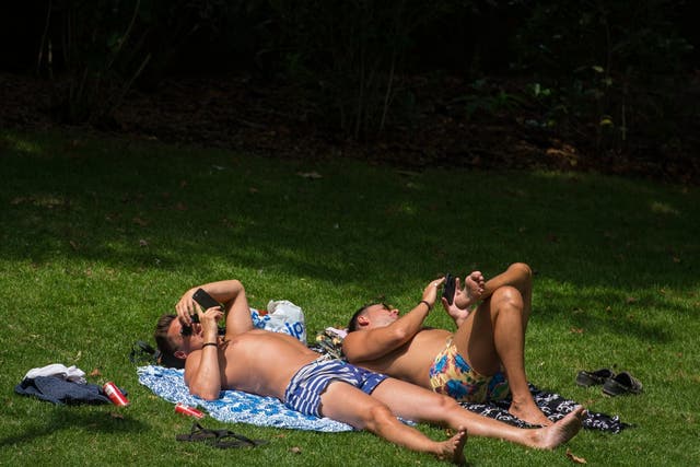 Two men lie in the sun in Embankment Gardens, central London, during hot weather in July