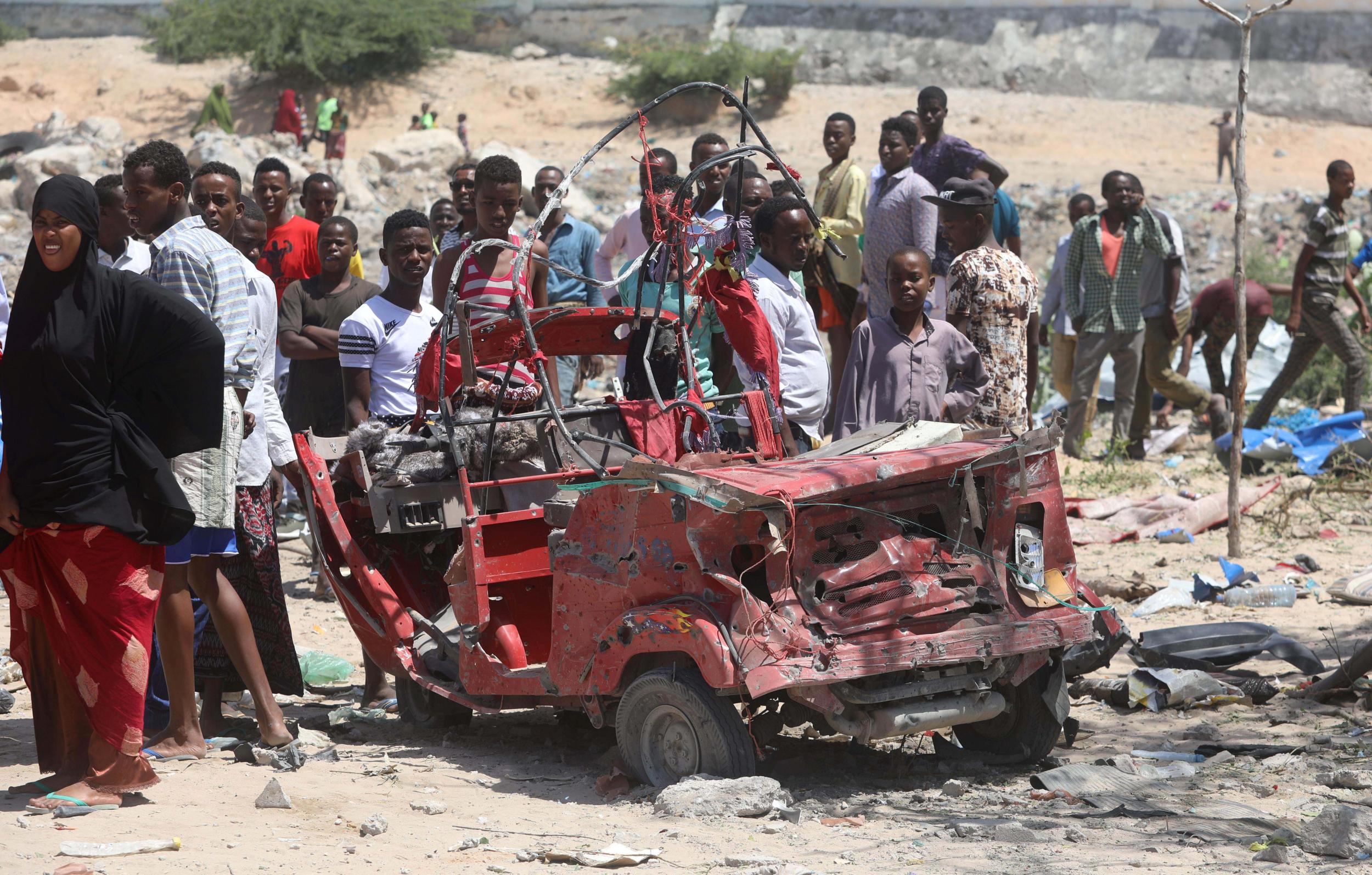 Civilians look at the remain of a rickshaw destroyed at the site of a blast in the district office of Hawlwadag in Mogadishu, Somalia.