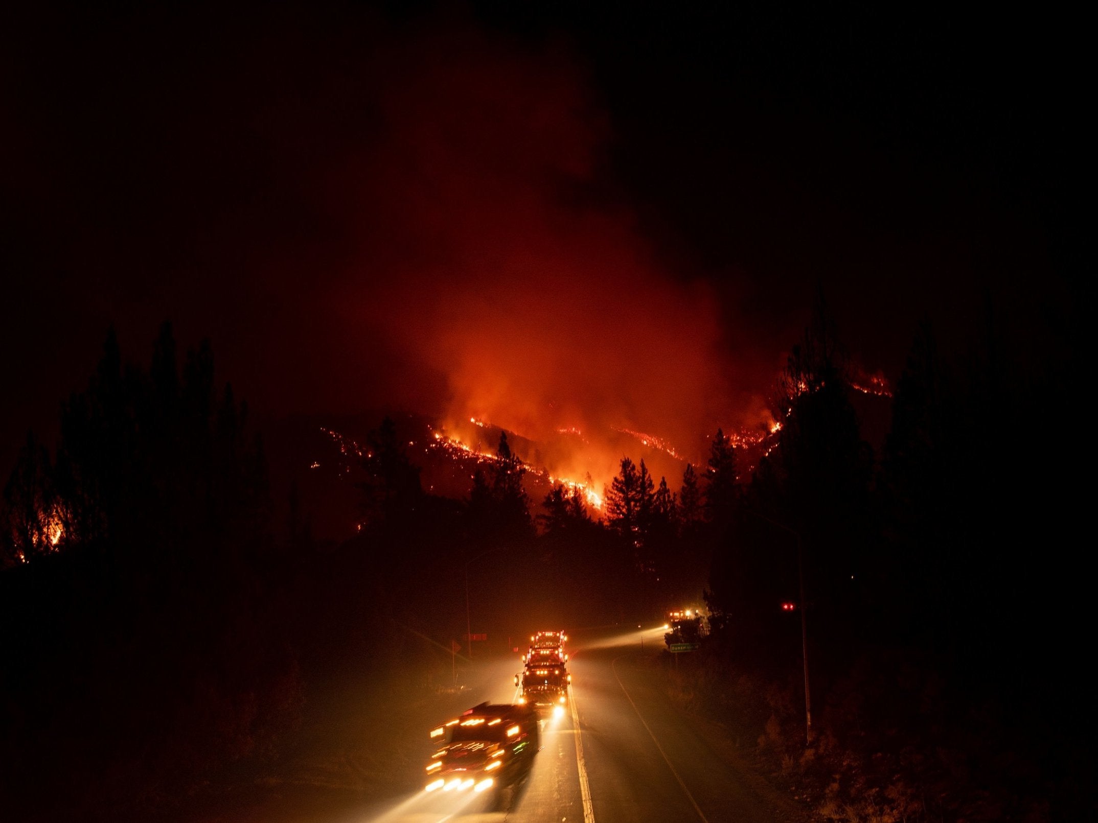 Fire trucks drive away from a burning hillside during the Delta Fire in California