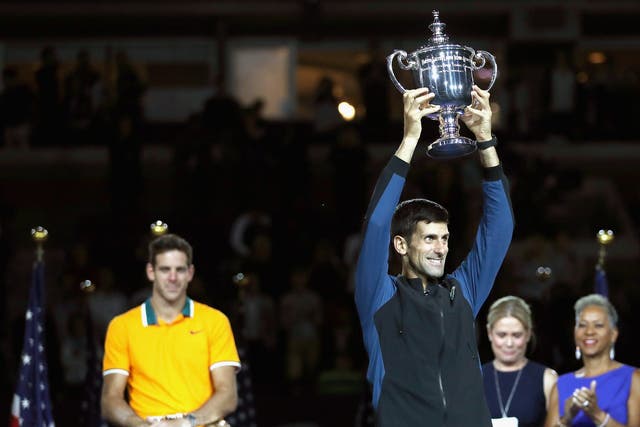 Djokovic poses with the championship trophy after winning his men's Singles finals match as Juan Martin del Potro looks on