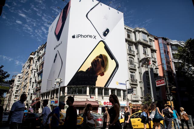 People cross the street underneath a billboard advertising the Apple iPhone X on August 15, 2018 in Istanbul, Turkey