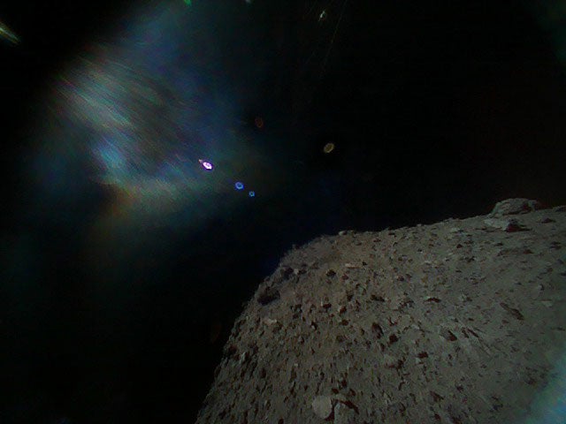 Image captured by one of the rovers taken immediately after separation from the spacecraft. The surface of Ryugu is in the lower right. The coloured blur in the top left is due to the reflection of sunlight when the image was taken.