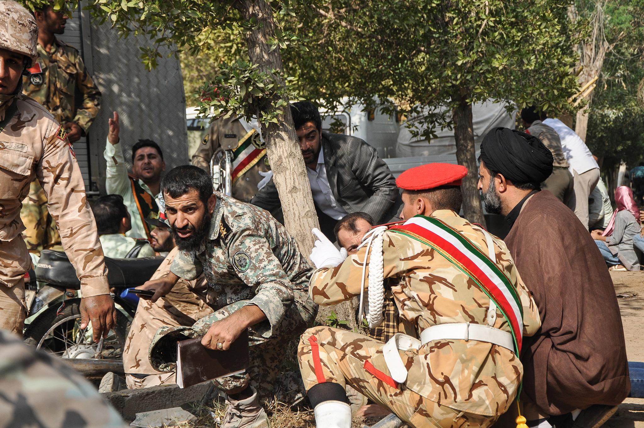 Soldiers and a cleric sit close to the ground seeking cover at the scene of an attack on a military parade in Ahvaz in September