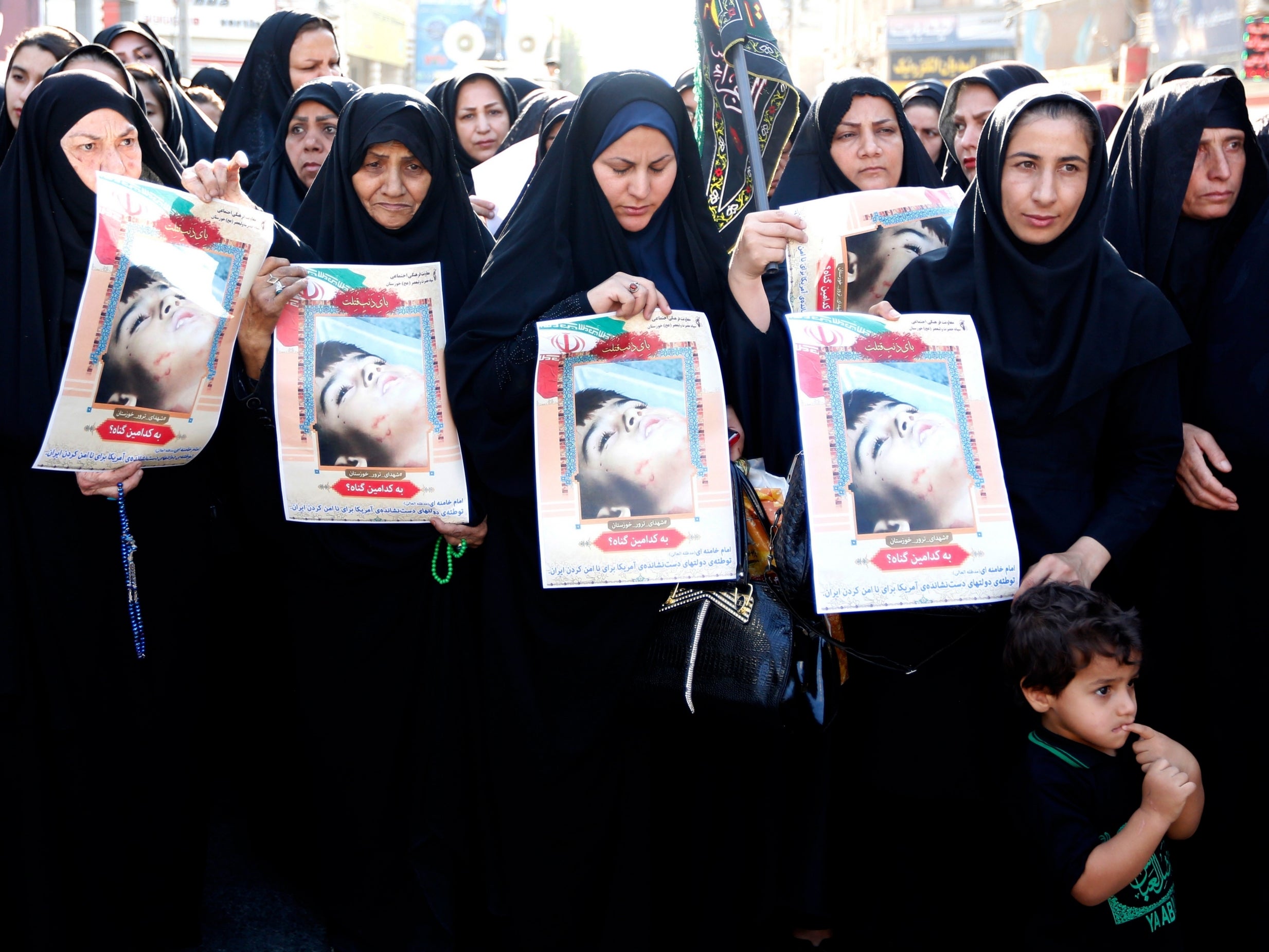 Iranian women hold pictures of a child who was killed in Saturday's attack during a funeral ceremony in Ahvaz yesterday