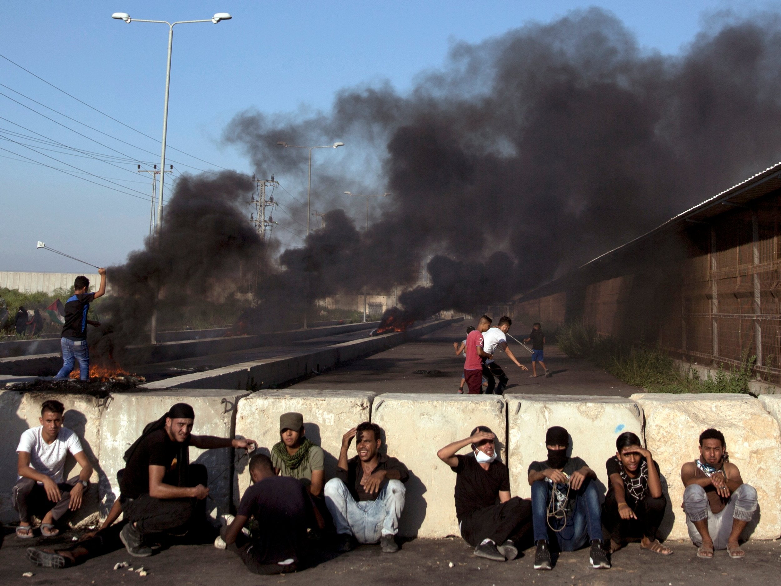 Palestinian protesters rest behind concrete blocks as others hurl stones at Israeli soldiers during a protest at the entrance of the Erez border crossing between Gaza and Israel, in the northern Gaza Strip on Wednesday, 26 September