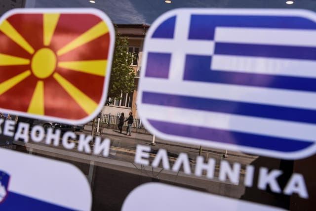People are reflected on a window bearing the flags of Macedonia and Greece in the town of Tetovo, near Skopje