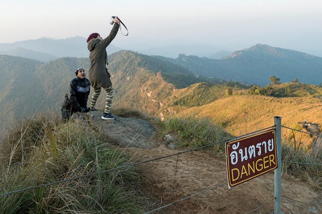 A couple ignore the danger sign to take selfies on a precarious ledge in Thailand’s mountainous Phu Chee Fah area