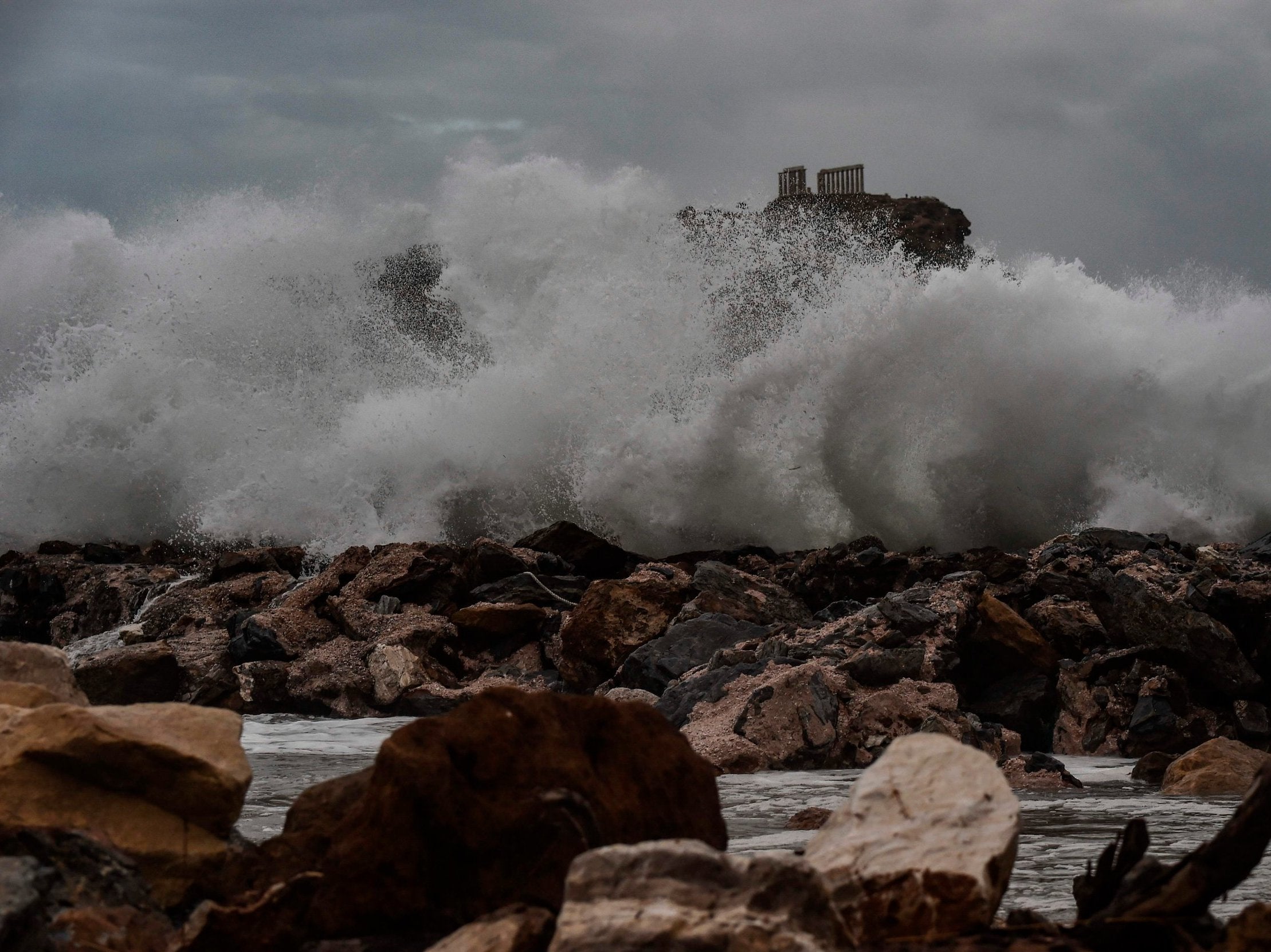 Waves hit the cliffs in front of the ancient Temple of Poseidon at cape Sounion, in southern Athens during bad weather