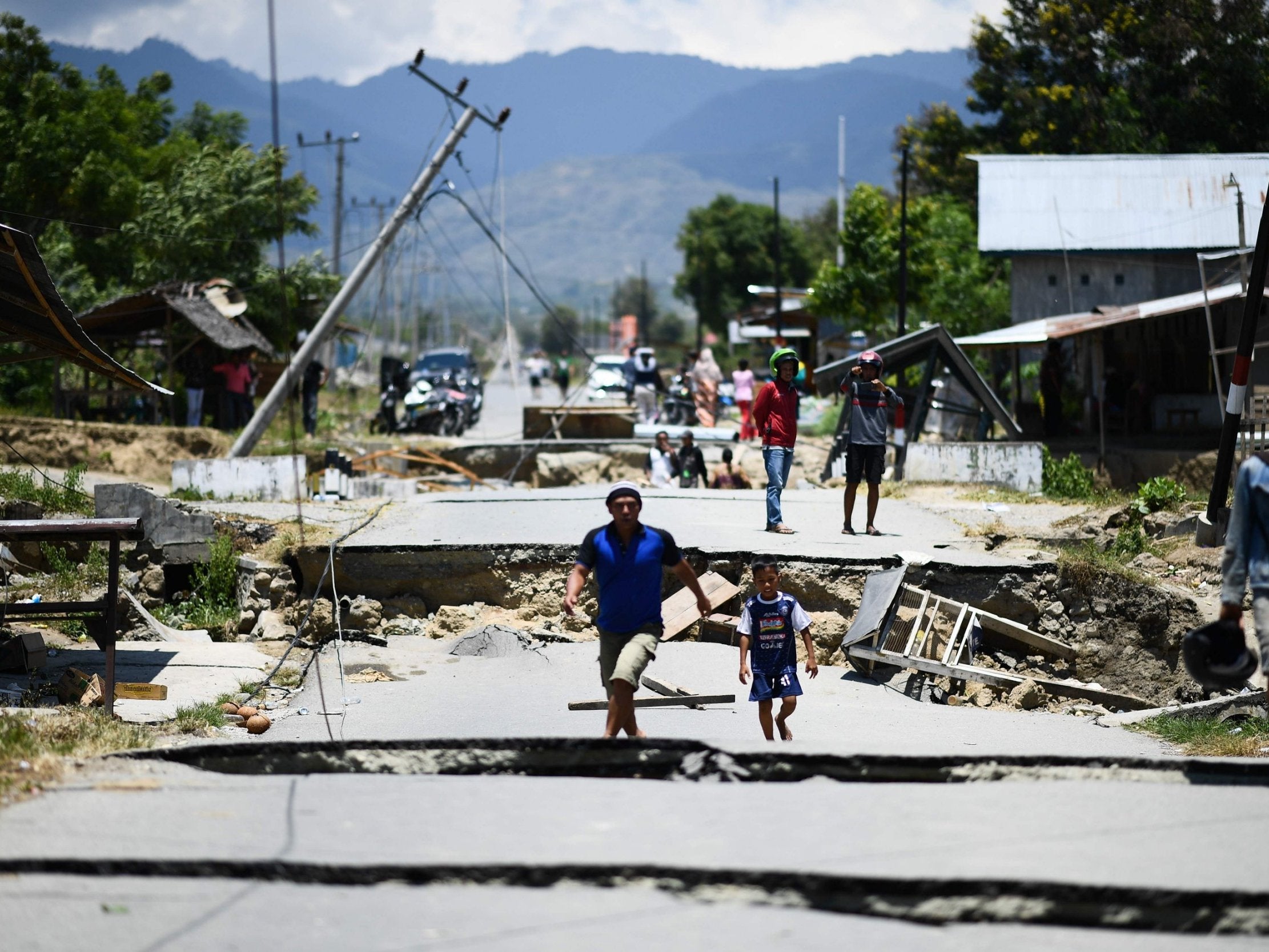 Survivors walk on a damaged street outside the city of Palu. The death toll in Indonesia has risen to 1,234 but is expected to go up as rescuers reach more villagers