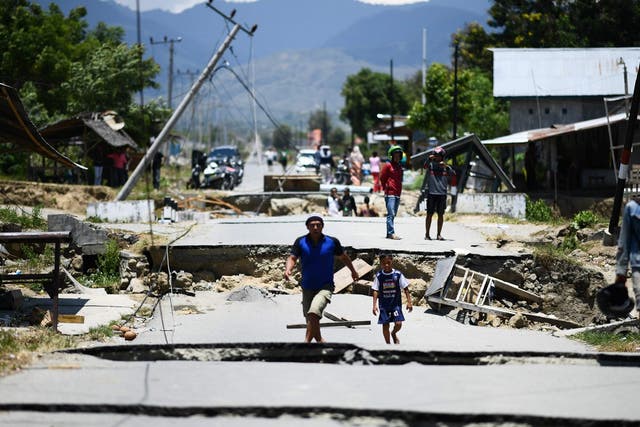 Survivors walk on a damaged street outside the city of Palu. The death toll in Indonesia has risen to 1,234 but is expected to go up as rescuers reach more villagers