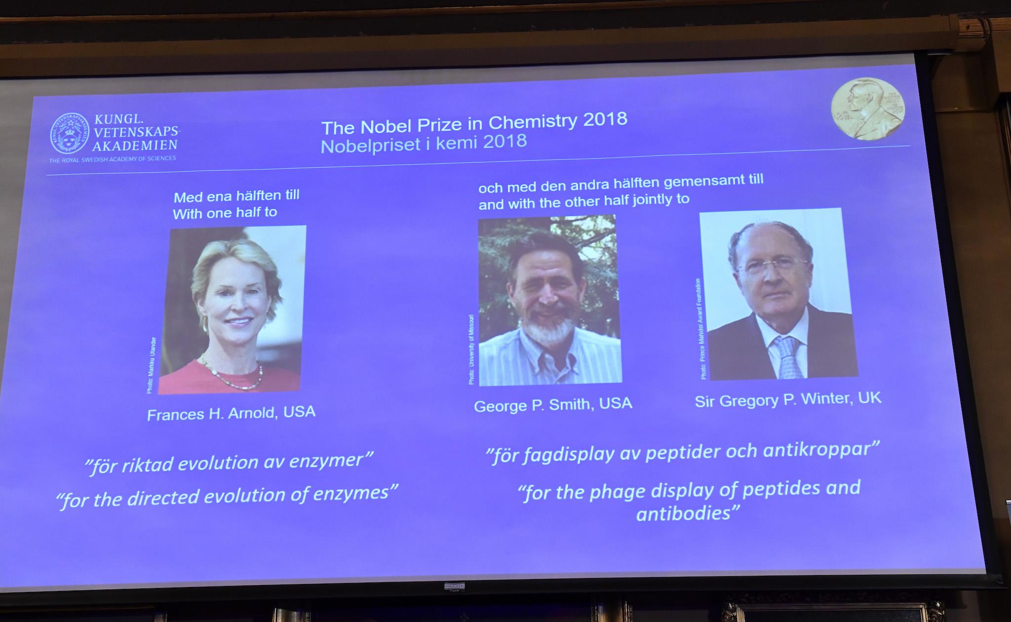 A screen displays portraits of Frances H Arnold of the United States, George P Smith of the United States and Gregory P Winter of Great Britain during the announcement of the winners of the 2018 Nobel Prize in Chemestry at the Royal Swedish Academy of Sciences on October 3, 2018 in Stockholm