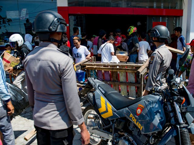 Police watch as people loot a convenience store in Palu, Sulawesi, on Sunday